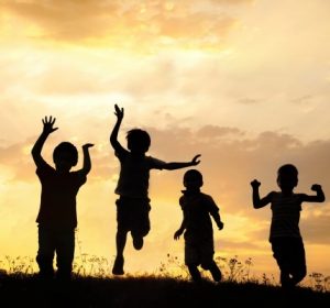 Silhouette group of happy children playing on meadow sunset